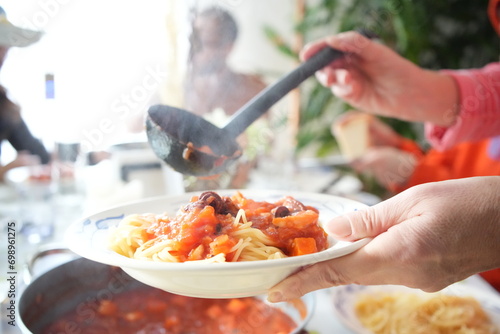 A woman pours a rich tomato sauce onto a plate of steaming pasta, the vibrant colors and textures inviting the viewer to indulge in a delicious Italian meal.