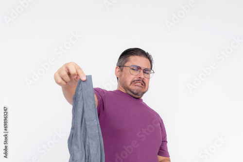 A middle aged man winces in disgust while holding a pair of smelly and dirty underwear as far from his face as possible. Isolated on a white background.