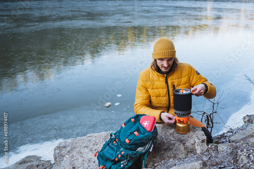 Guy cooking outdoors on a gas burner, capming by the lake, cooking in winter in the forest, outdoor recreation, camping equipment for hiking. photo
