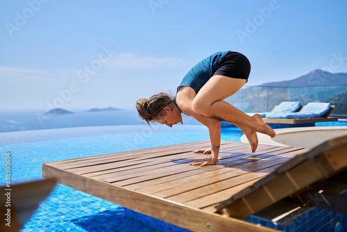 Woman doing yoga on deck chair near swimming pool photo