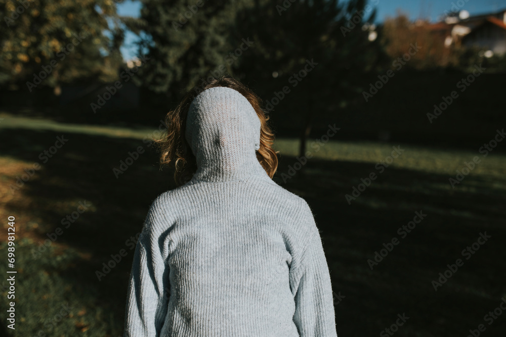 Woman covering face with hooded shirt in autumn park at sunset Woman covering face with hooded shirt in autumn park at sunset
