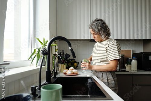 Mature woman pouring juice into glass at home