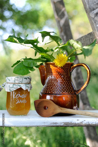 Jar of jam, wooden ladle and dandelion in ceramic jug photo
