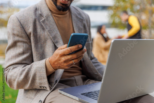 Businessman sitting with laptop and using smart phone at office park photo