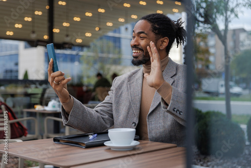 Happy businessman waving hand on video call through smart phone at cafe photo