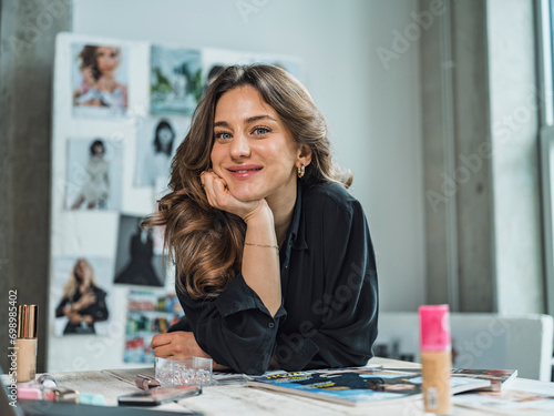 Smiling freelancer sitting with beauty products at desk in studio photo