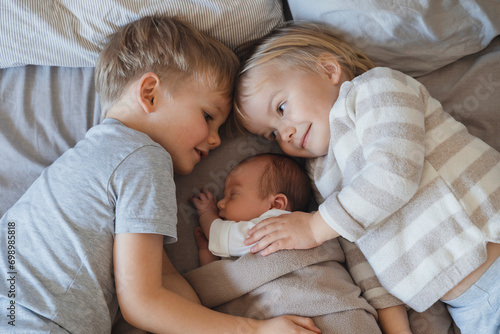 Newborn baby boy sleeping near siblings lying in bed photo