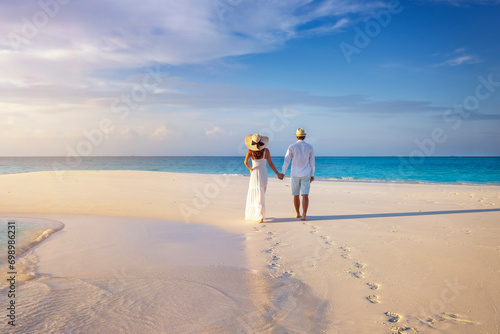 A beautiful couple holding hands walks down a tropical paradise beach during sunset time photo