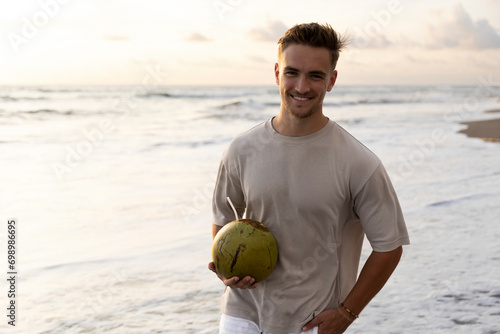 Smiling young man holding fresh coconut in hand at beach photo
