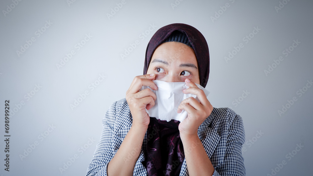 Asian Islamic businesswoman feeling sick and blowing nose while working in the office. Asian Islamic businesswoman feeling sick and blowing nose while working in the office.