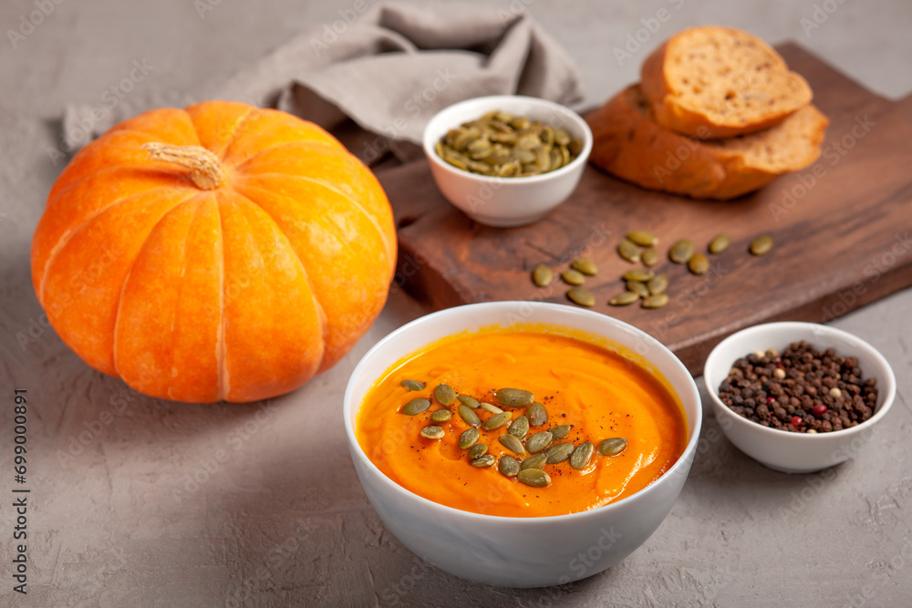 Pumpkin soup with seeds, spices, pepper and bread on a gray background. The concept of healthy vegetable soups. Concept of healthy eating or vegetarian food. Healthy seasonal autumn cuisine Pumpkin soup with seeds, spices, pepper and bread on a gray background. The concept of healthy vegetable soups. Concept of healthy eating or vegetarian food. Healthy seasonal autumn cuisine