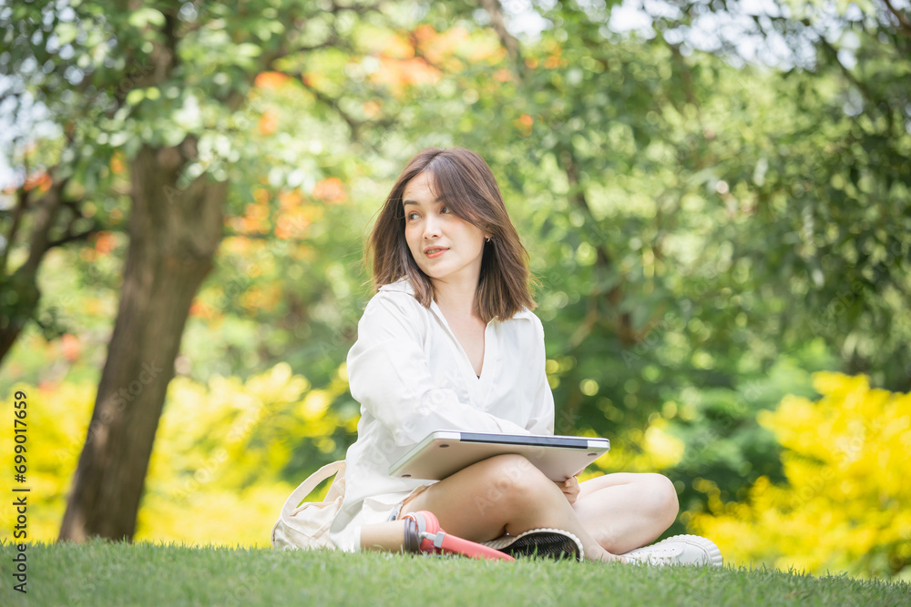 Young freelancer with laptop and headphones in a green park. Cheerful modern woman sitting outdoors in the park on grass and using a laptop computer while drinking takeaway coffee Young freelancer with laptop and headphones in a green park. Cheerful modern woman sitting outdoors in the park on grass and using a laptop computer while drinking takeaway coffee