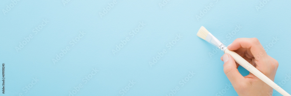 Girl hand holding paintbrush on light blue wall background. Pastel ...