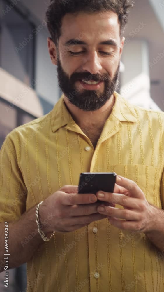Vertical Screen: Portrait of Young Man in Casual Clothes Walks in Corporate Office Hallway, Using his Smartphone and Smiling. Successful Businessman Communicating with Colleagues Over Text Messages Vertical Screen: Portrait of Young Man in Casual Clothes Walks in Corporate Office Hallway, Using his Smartphone and Smiling. Successful Businessman Communicating with Colleagues Over Text Messages