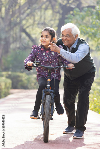 Photography Grandfather assisting playful granddaughter in riding bicycle at park