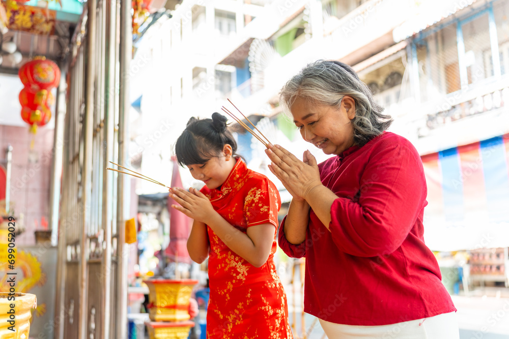 Chinese lunar new year festival and tradition holiday celebration concept. Happy Asian family grandmother and grandchild girl praying a wish with incense and red candle together at Chinese shrine. - obrazy, fototapety, plakaty 
