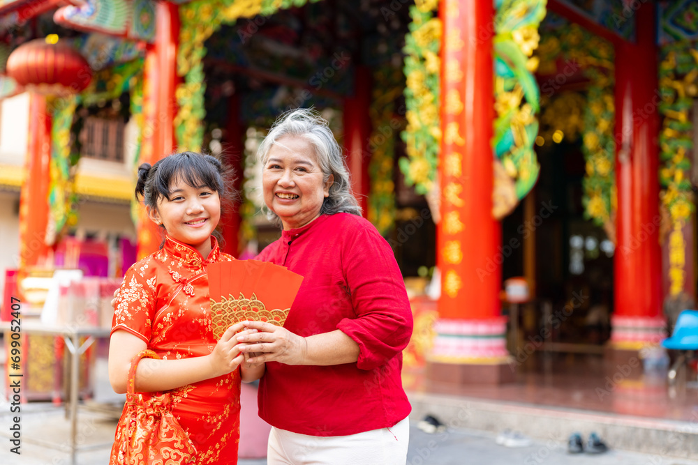 Chinese lunar new year festival and tradition holiday celebration concept. Happy Asian family grandmother giving red envelope contained money gift with blessing to little grandchild girl in red dress.