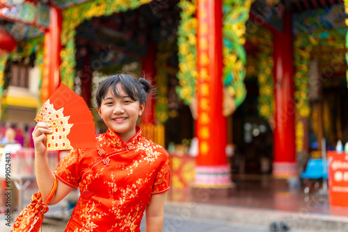 Chinese lunar new year festival and tradition holiday celebration concept. Happy Little Asian girl in Chinese red dress holding money gift in red envelopes in front of in Chinese temple shrine.
