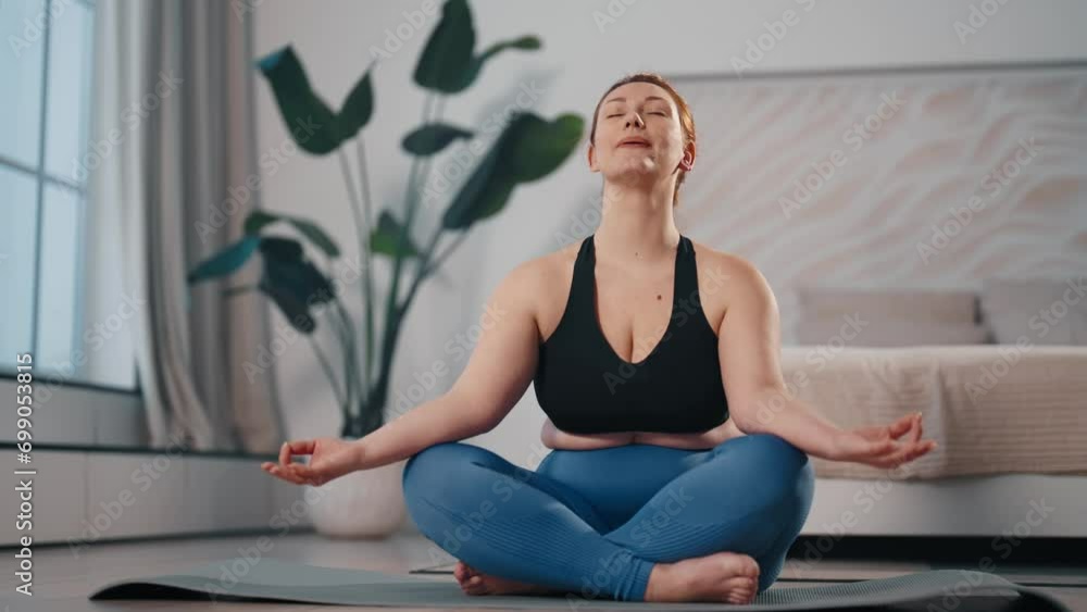 Woman meditating in lotus pose at home.Middle aged female ending yoga practice meditation sitting on mat deeply breathing with closed eyes feeling harmony. Sport active lifestyle, spiritual practice. Woman meditating in lotus pose at home.Middle aged female ending yoga practice meditation sitting on mat deeply breathing with closed eyes feeling harmony. Sport active lifestyle, spiritual practice.