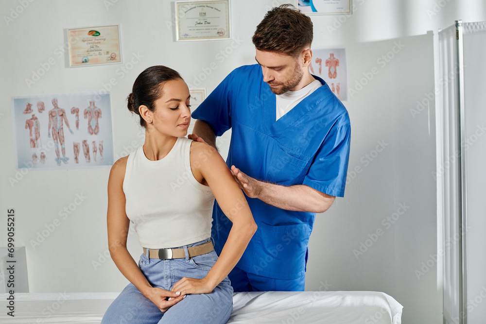 Obraz premium handsome doctor in blue medical costume massaging shoulder of his young attractive patient