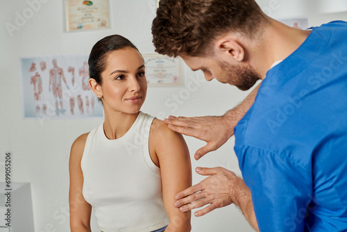 beautiful young woman looking at her bearded doctor while he checking her shoulder, healthcare