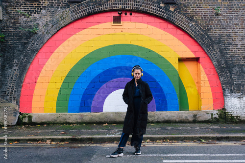 Woman wearing wireless headphones and standing in front of rainbow wall photo