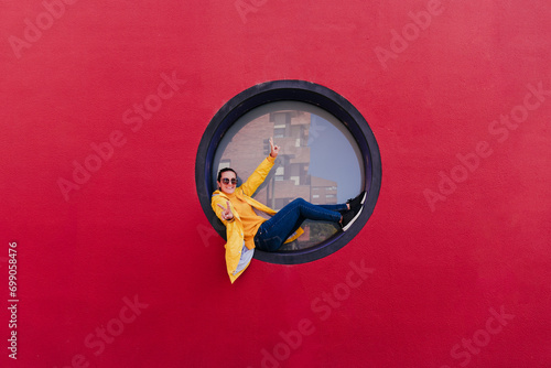 Woman in yellow rain coat sitting in porthole making victory sign photo