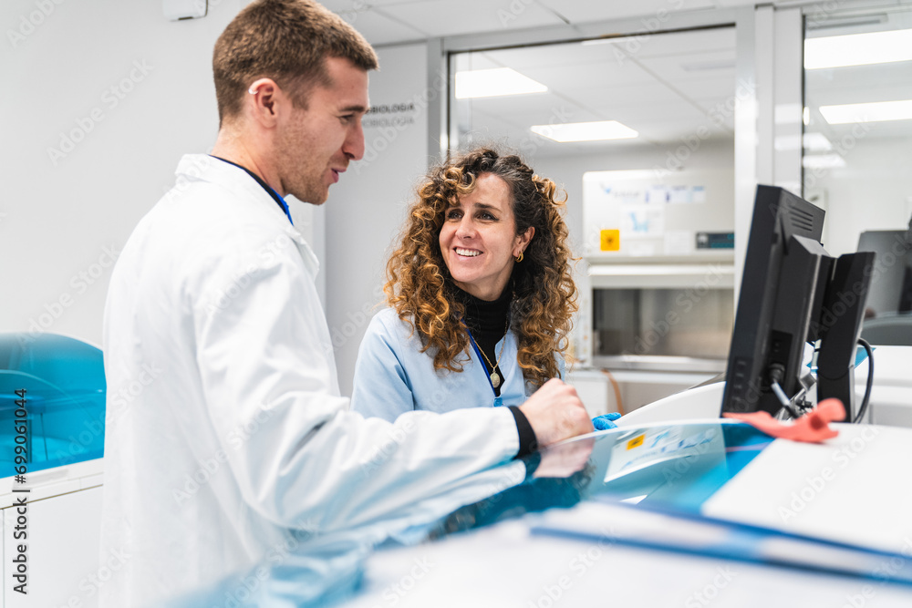 Obraz premium Two medical experts engage in a detailed review of blood tests within the high-tech environment of a hospital's clinical laboratory.