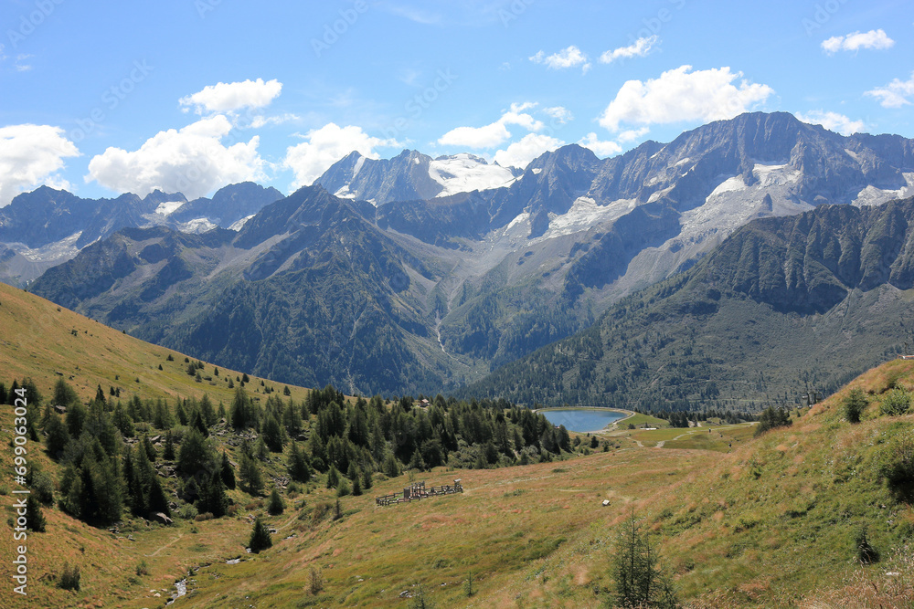 Landscape with fields, lake and mountains in the Italian Alps, under a brilliant sunny an cluody sky Landscape with fields, lake and mountains in the Italian Alps, under a brilliant sunny an cluody sky