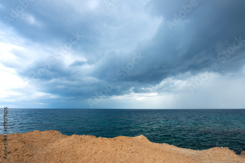 Looking at the sea from the coastal green area. Looking at the sea from the rocks on a cloudy day. Sea view from red cliffs.Cyprus coast.