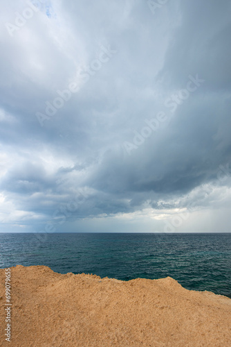 Looking at the sea from the coastal green area. Looking at the sea from the rocks on a cloudy day. Sea view from red cliffs.Cyprus coast.