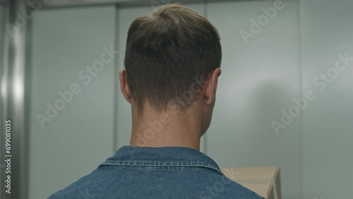 Back view of man walking out of elevator and bringing cardboard boxes to self service warehouse photo