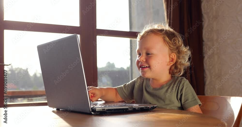 Little boy is engrossed in online learning activity on laptop, pointing at screen with enthusiasm. He then turns his head to look straight at camera, his expression reflecting his engagement Little boy is engrossed in online learning activity on laptop, pointing at screen with enthusiasm. He then turns his head to look straight at camera, his expression reflecting his engagement