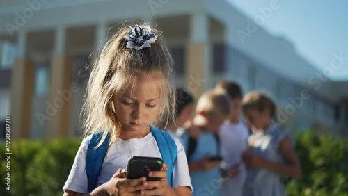 Children stand in schoolyard and look at smartphone.students with backpacks at school.children play smartphones in school yard after school.students listen to music on smartphone.happy family concept photo