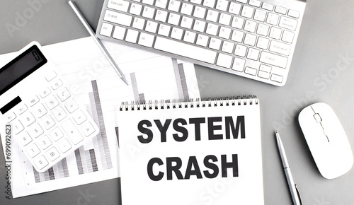 SYSTEM CRASH text written on notebook on grey background with chart and keyboard, business concept