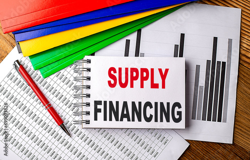 SUPPLY FINANCING text on notebook with pen, folder on a chart background