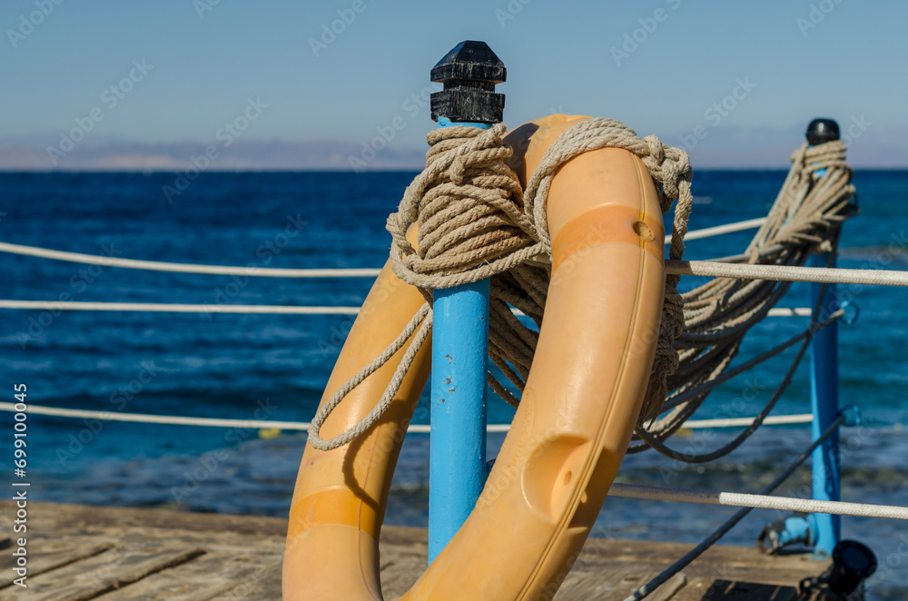 orange lifebuoy on a wooden table with ropes on a wooden platform on a background of blue sea in Egypt Dahab South Sinai