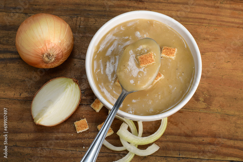 onion soup, onion cream in a white bowl, a spoon with a portion of onion cream, wooden bottom