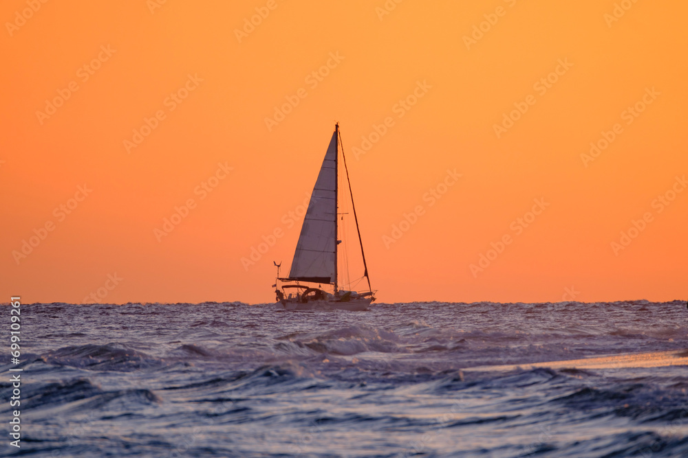 Beautiful bright orange sunset and a sailboat sailing on the ocean near the Canary Island of Fuerteventura, Spain.