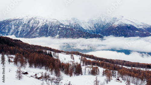 Aerial view of winter landscape with mountain peaks covered with snow, fluffy clouds and coniferous forest. Natural background.