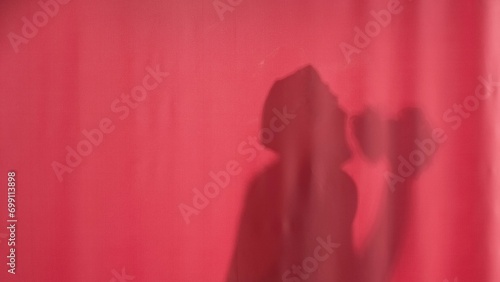 Silhouette of a man washing behind a pink curtain. Man in waterproof cap washing, dancing and singing, using loofah as a microphone. Body washing.