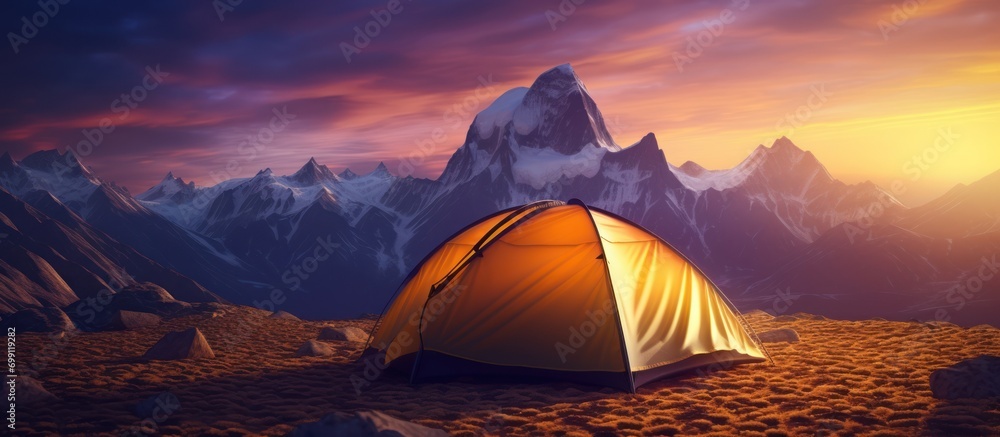 The dome tent is illuminated by the warm light of the rising sun as the golden cloudscape reveals dramatic mountain peaks from a panoramic landscape with blue, purple and orange skies - obrazy, fototapety, plakaty 