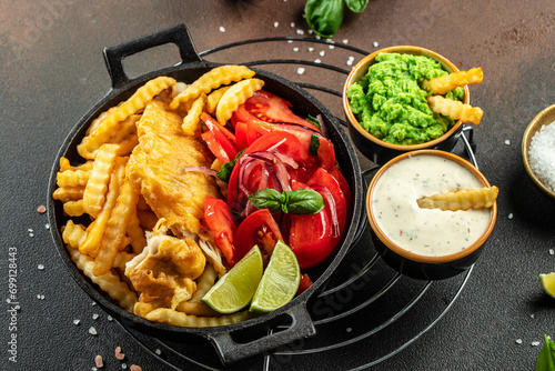 Authentic traditional British cuisine fish and chips served with mashed peas, vegetable salad, tartar sauce. top view photo