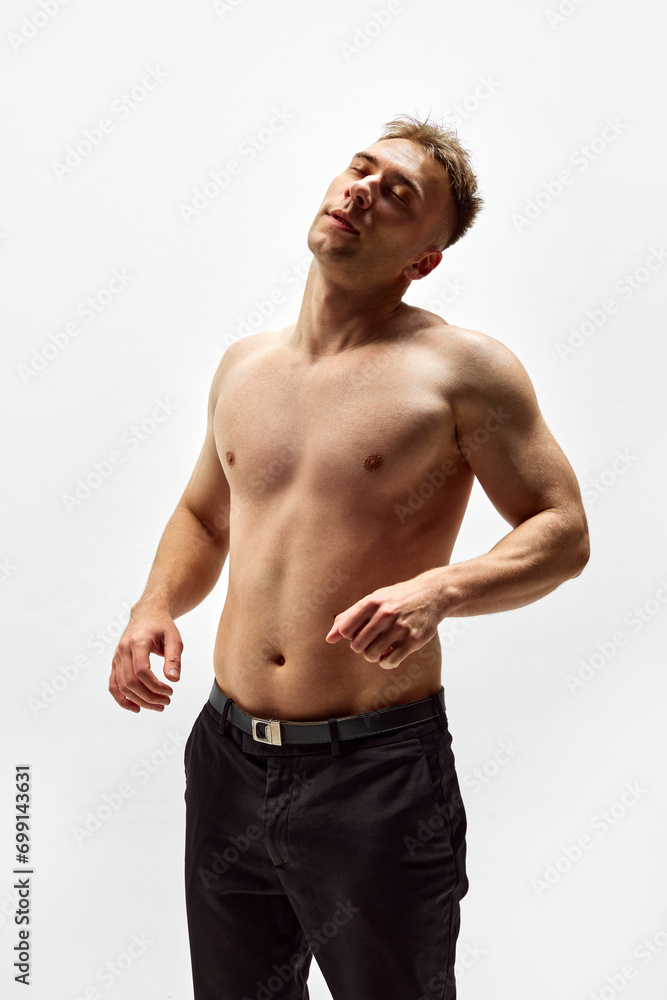 Neck stretch. Shirtless muscular young man with fit string body standing in pants isolated over white studio background. Concept of male beauty, body care, fitness, sport, health Neck stretch. Shirtless muscular young man with fit string body standing in pants isolated over white studio background. Concept of male beauty, body care, fitness, sport, health