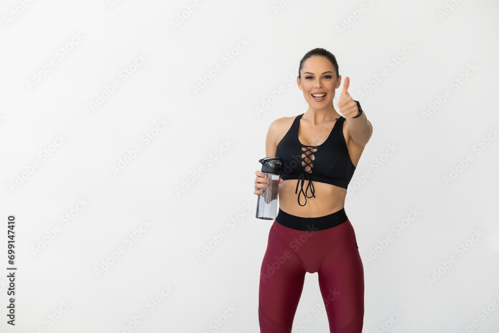 Portrait of cheerful young attractive woman showing thumbs up gesture, with bottle of water, at gym Portrait of cheerful young attractive woman showing thumbs up gesture, with bottle of water, at gym