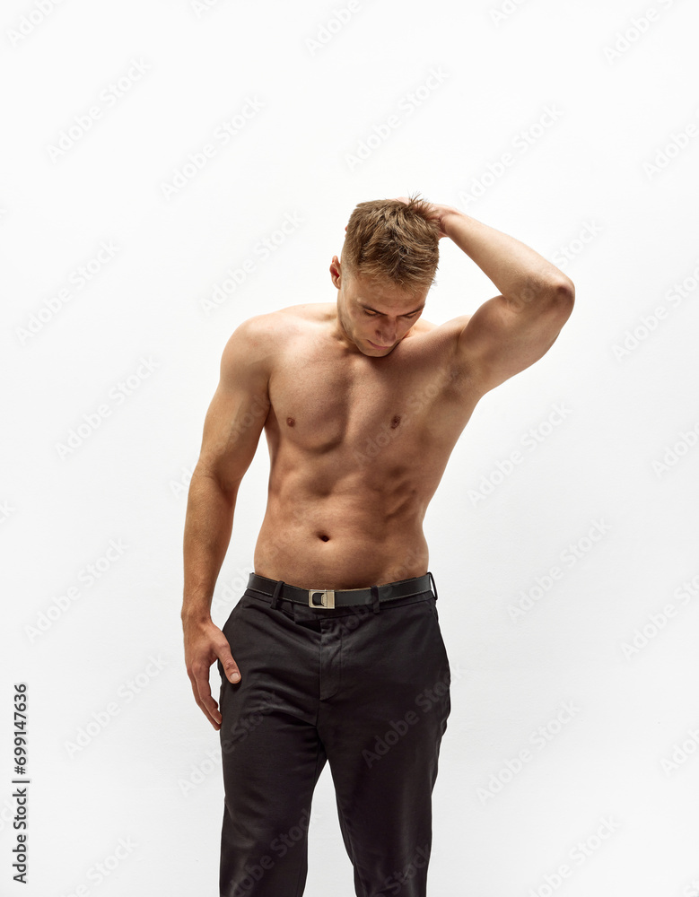 Handsome young man with shirtless, muscular body standing in pants isolated over white studio background. Relief torso. Concept of male beauty, body care, fitness, sport, healthy lifestyle