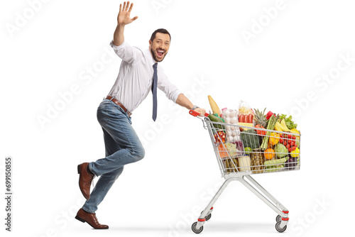 Cheerful man running with food in a shopping cart and waving at camera