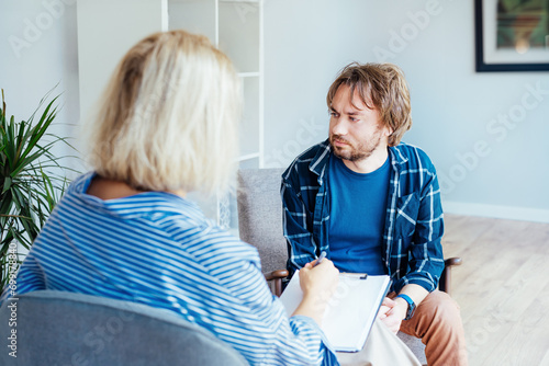 Depressed male patient having psychotherapy session with counselor at mental health clinic. Man with emotional problems consulting professional therapist i comfy office. Psychological help service. photo