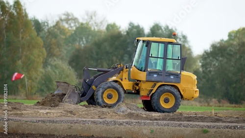 Small tractor move soil for landscaping purposes. Mini excavator leveling ground with front bucket on construction site. Bulldozer picks up huge pile of sand earth and clay in bucket