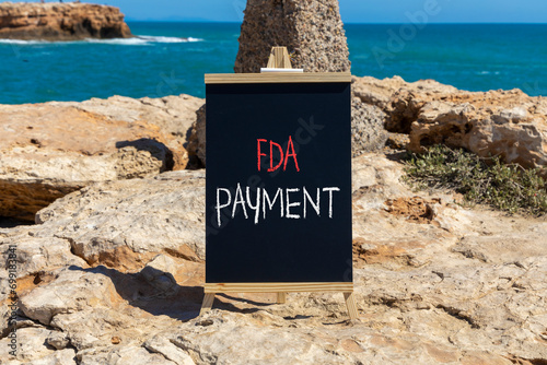 FDA Food and Drug Administration payment symbol. Concept words FDA payment on beautiful black chalk blackboard. Beautiful stone beach blue sea sky background. Business FDA payment concept. Copy space.